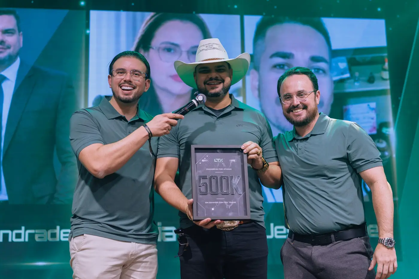Trader de chapéu com a placa de 500K entre dois mentores