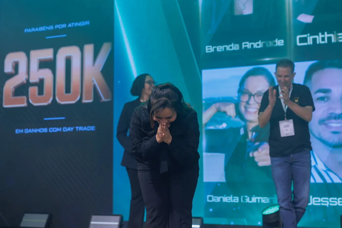 Trader no palco do LTX Summit, curvada, com as mãos juntas em gratidão