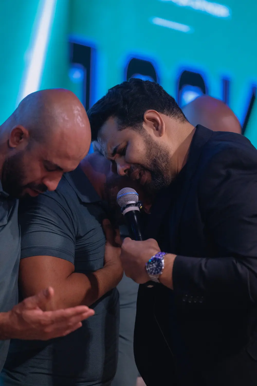 Dois homens de cabeça baixa orando juntos, um deles com as mãos abertas