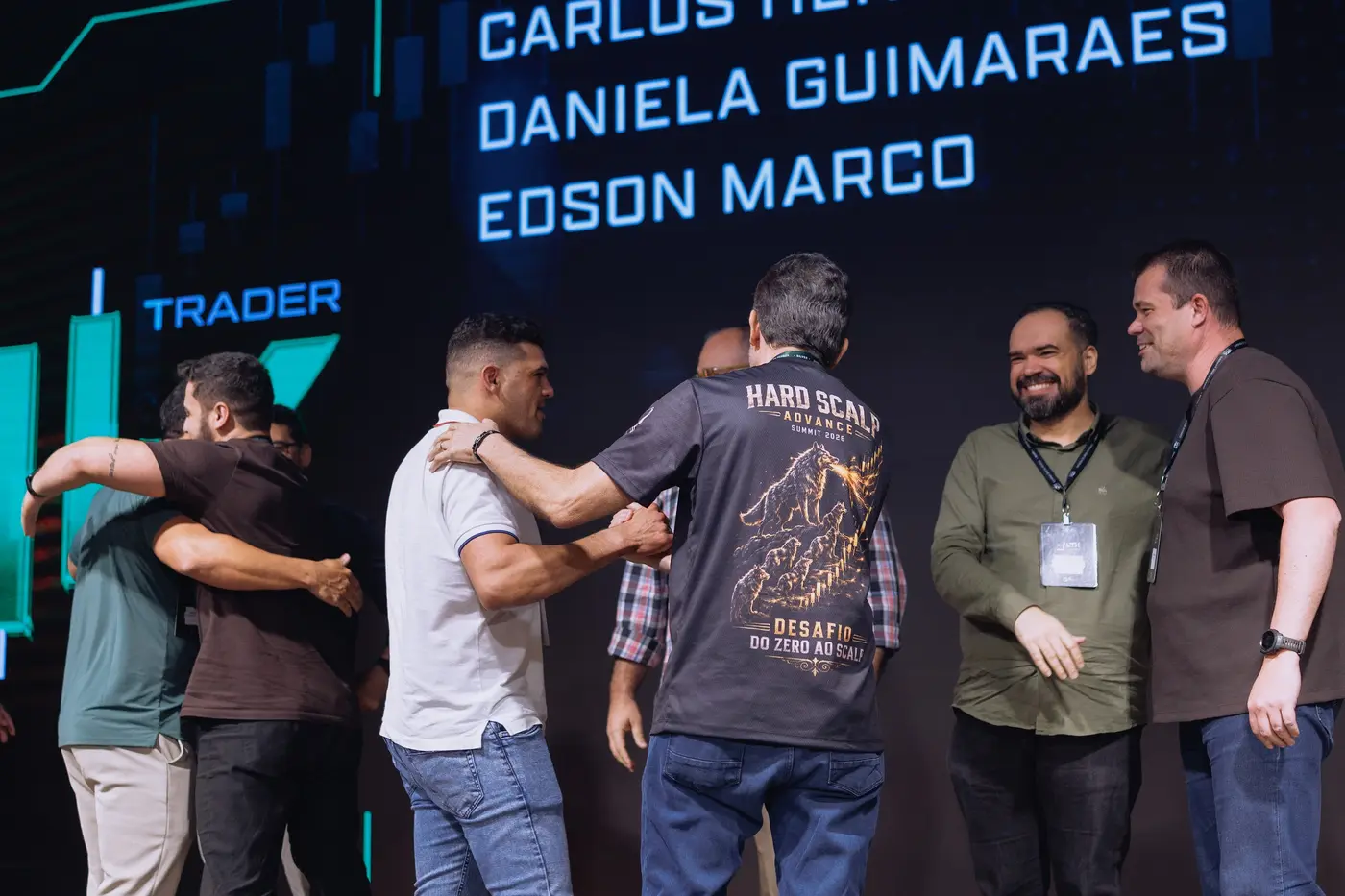 Abraços no palco diante do telão com os nomes dos alunos Trader 1K