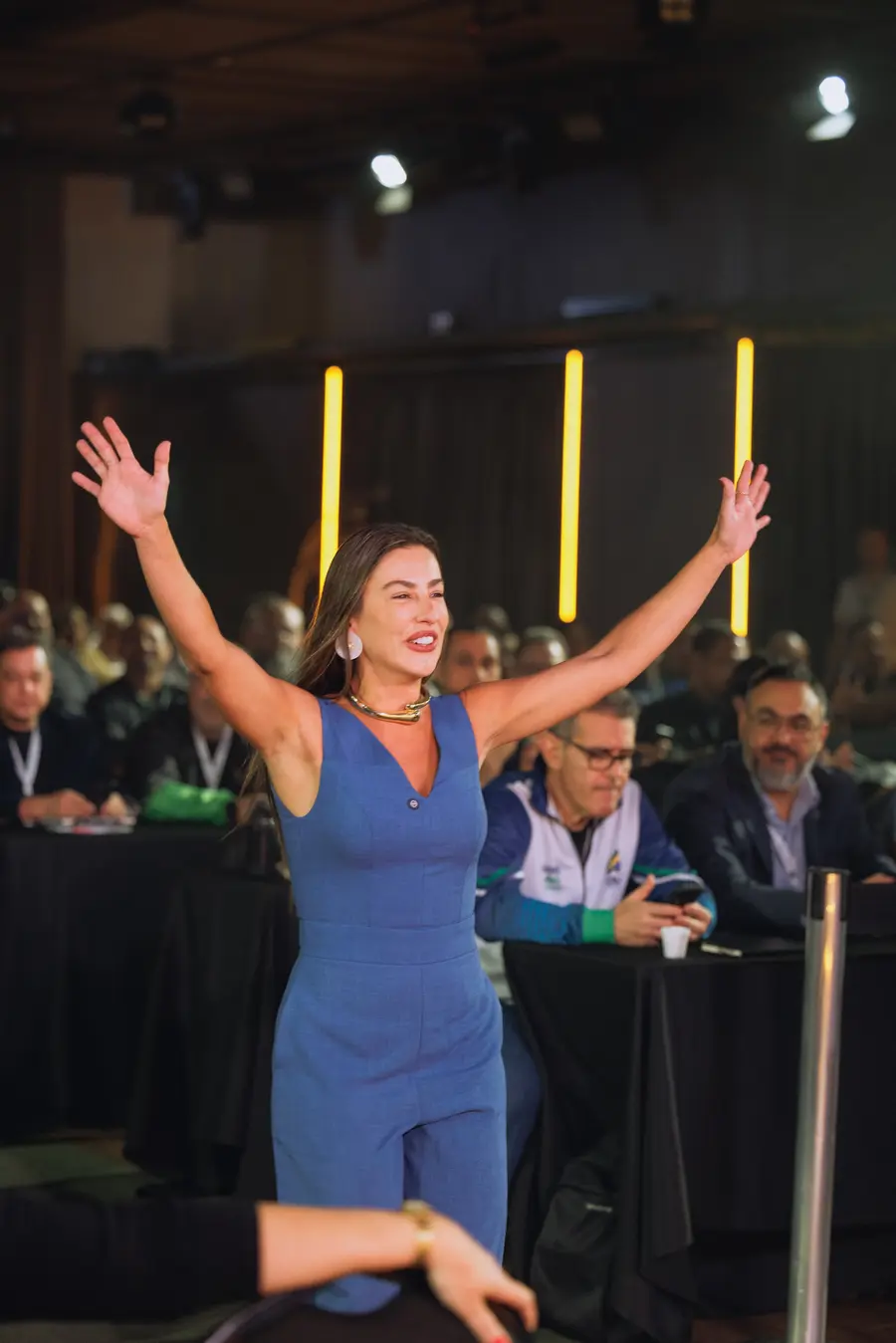 Participante de macacão azul comemorando com os braços abertos