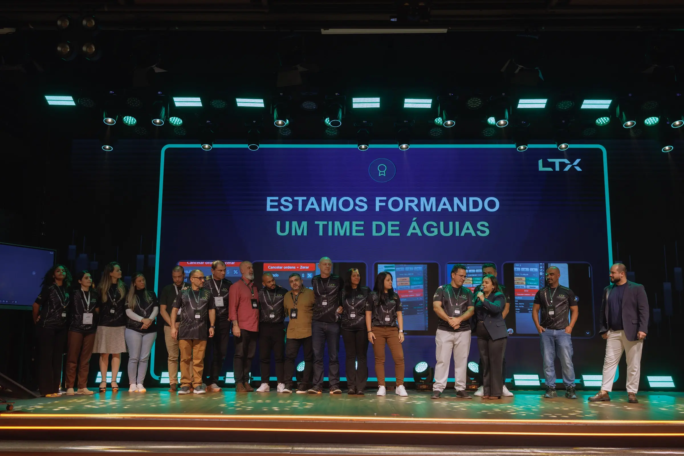 Turma de traders no palco do LTX Summit, embaixo do telão com a frase Estamos formando um time de águias