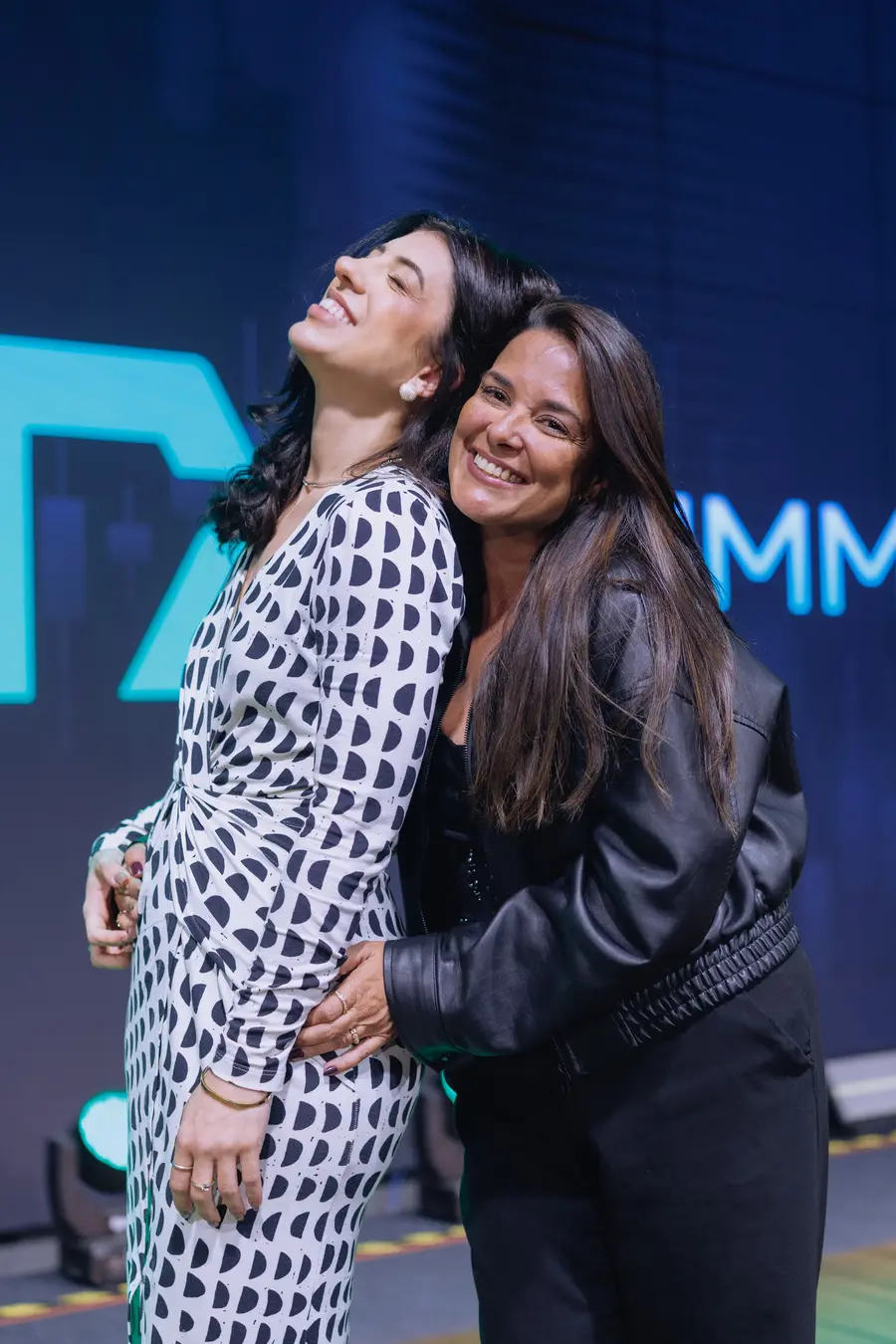 Duas amigas abraçadas e rindo diante do logo do Summit