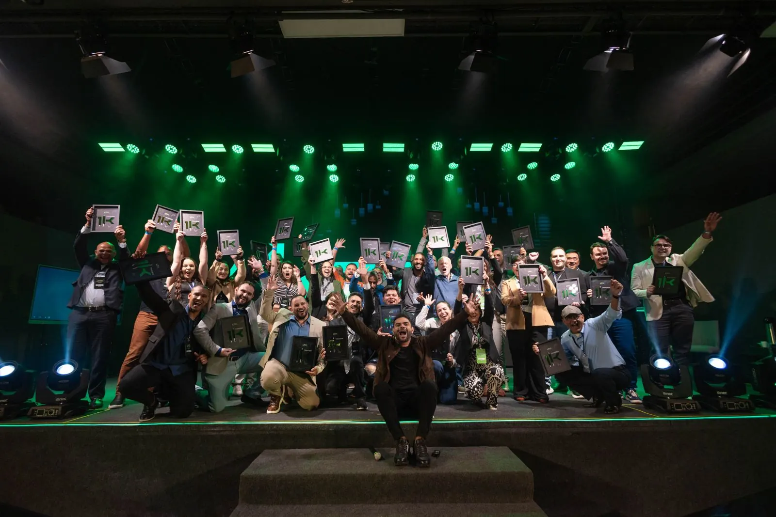 Turma da LTX comemorando no palco com as placas Trader 1K levantadas